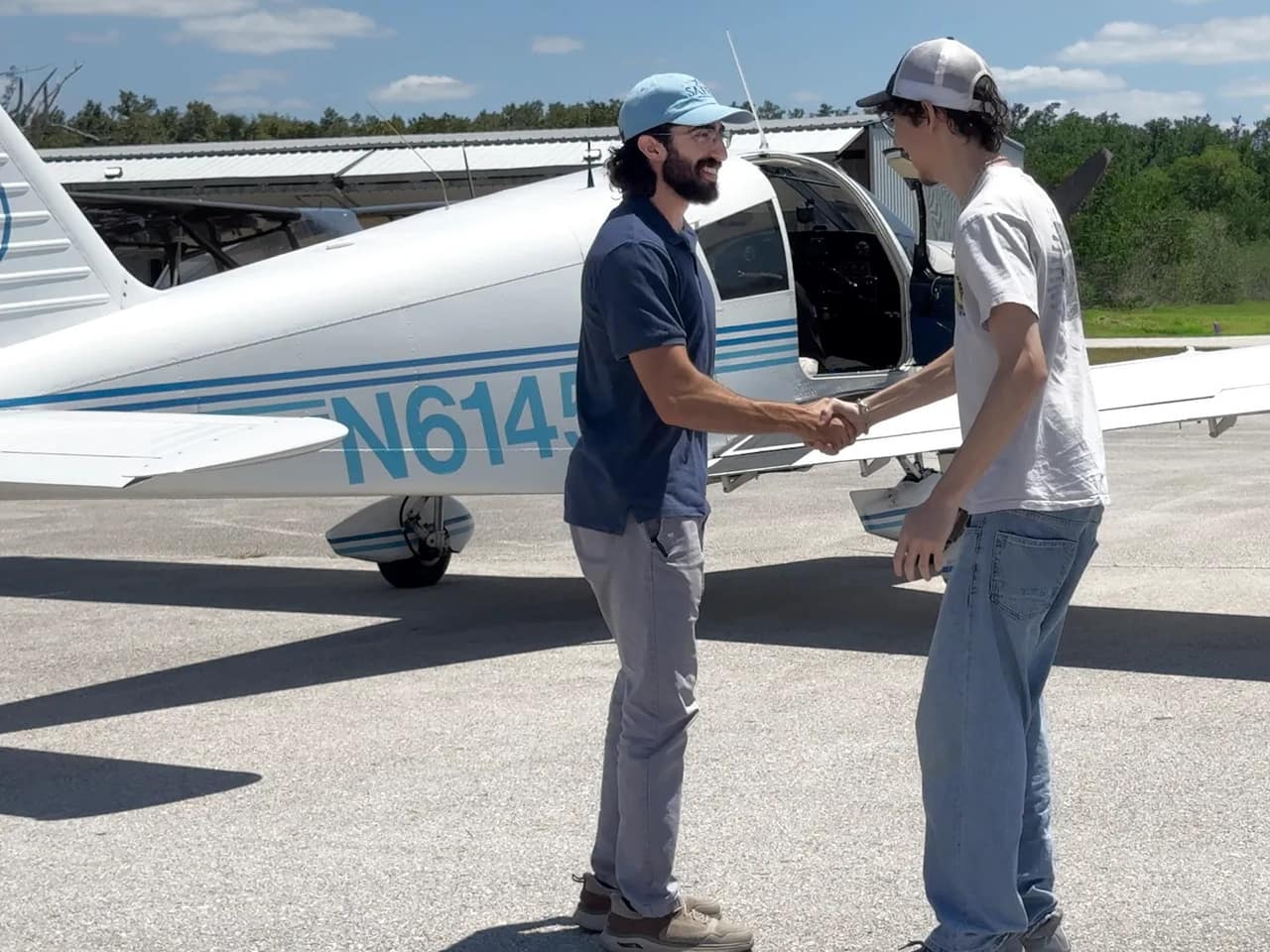 Flight instructor shaking hands with a student pilot beside the Cherokee 140 on the ramp